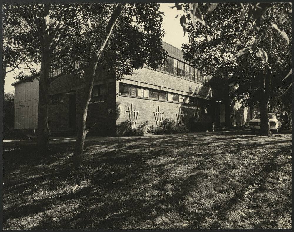 View Across Green to HK Ward Gymnasium Building with Cars Parked Across from the Entrance