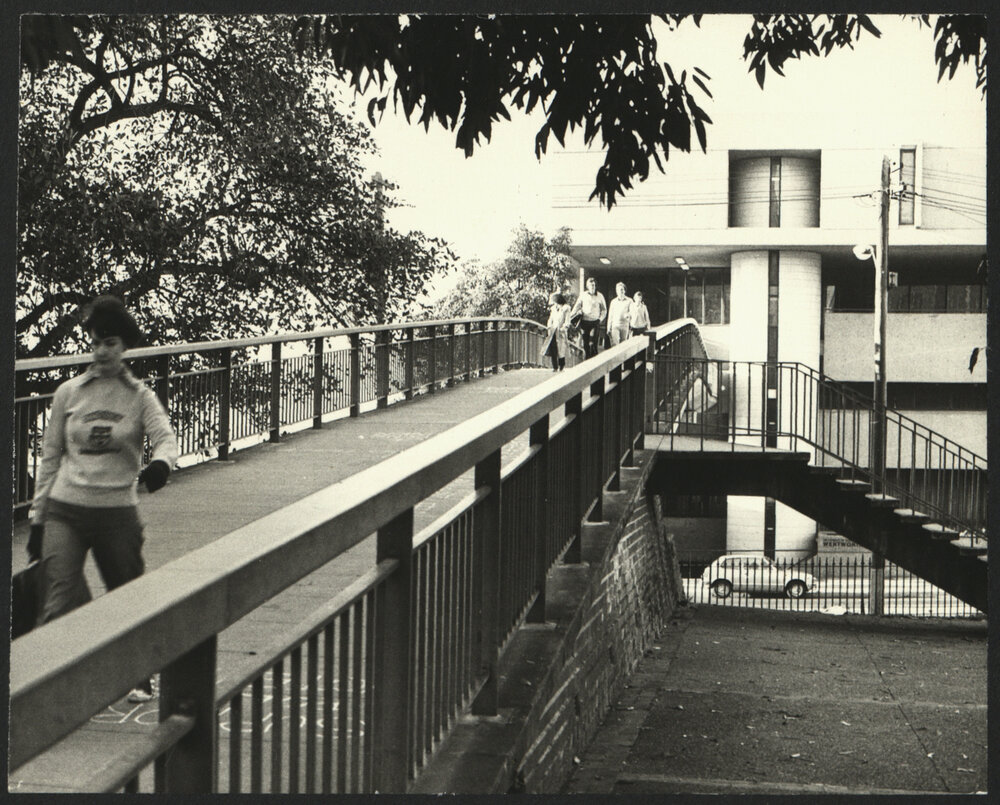 View from Campus Across the Footbridge Towards Wentworth Building with Students Crossing the Bridge
