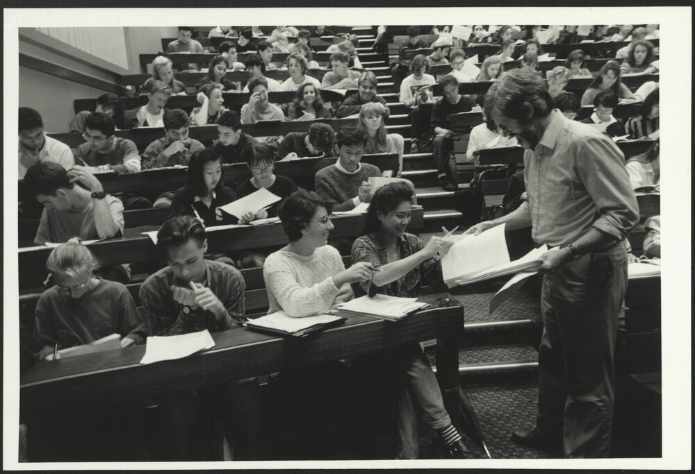 Students in Lecture Room with Lecturer Handing Out Papers