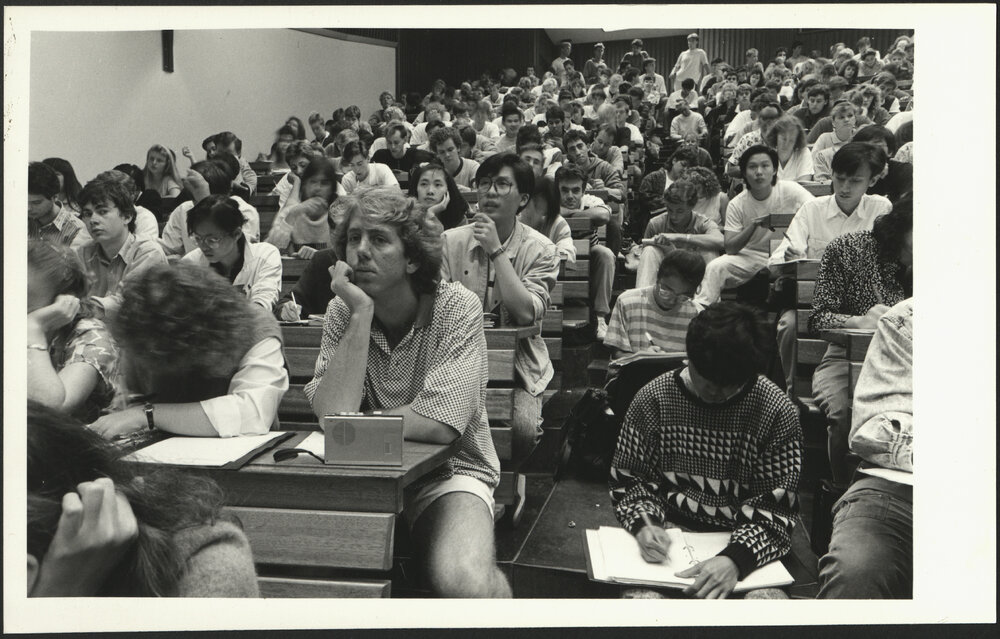Students Attending an Overcrowded Lecture Sitting on Stairs, Standing at Back