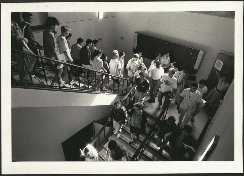 Students in Stairwell After Examination with Staff Member Holding a Sign 'Silence Examination in Progress'
