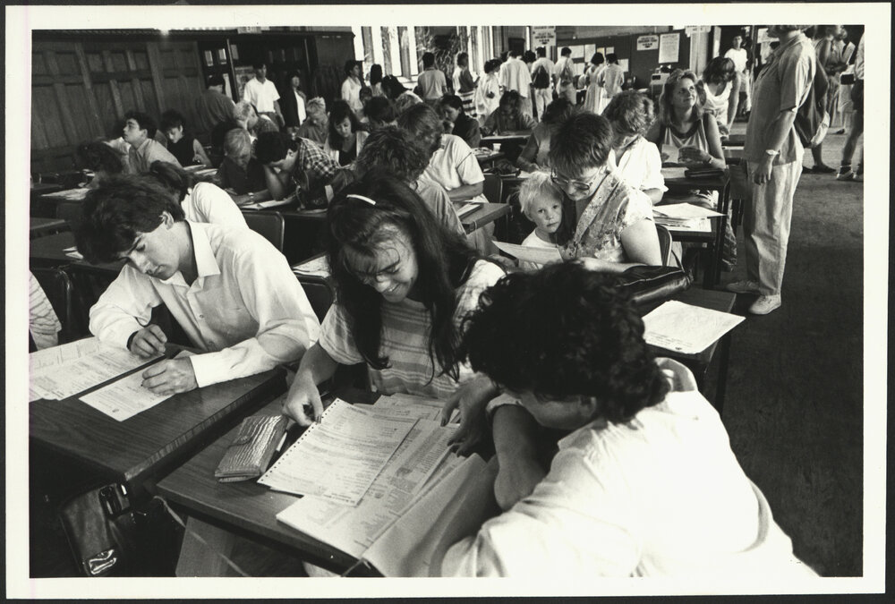Students Completing Enrolment Forms in MacLaurin Hall with One Student holding a Young Child on Her Lap