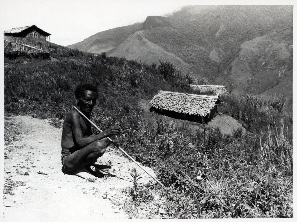 Man Crouching with Buildings on Mountainside in Background