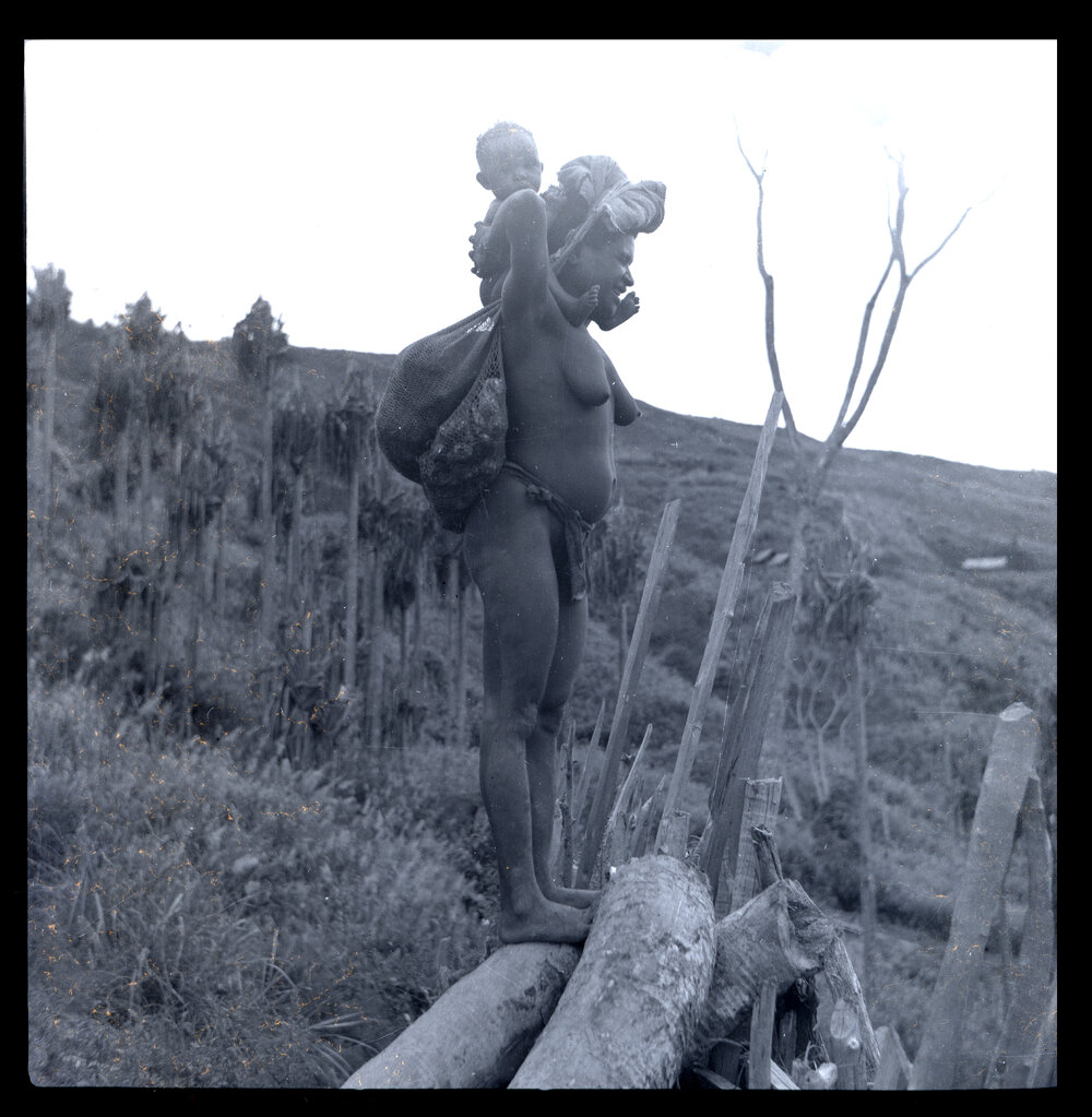 Woman Standing with Baby on Shoulders and Net Bags