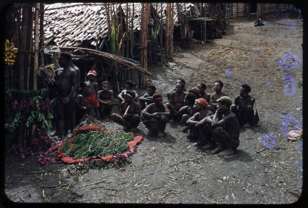 Group of Men Sitting at the Base of a Food Pole