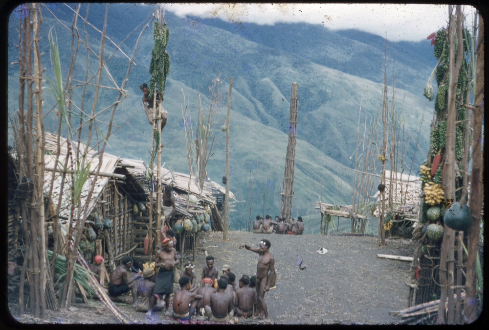 Group of Men Sitting at the Base of a Food Pole