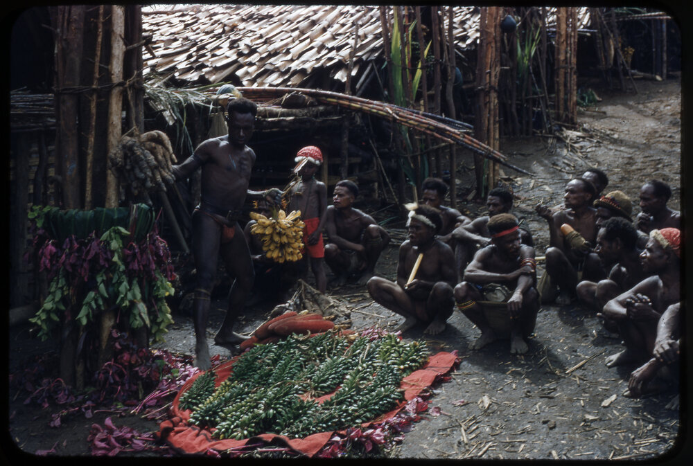 Group of Men Sitting at the Base of a Food Pole