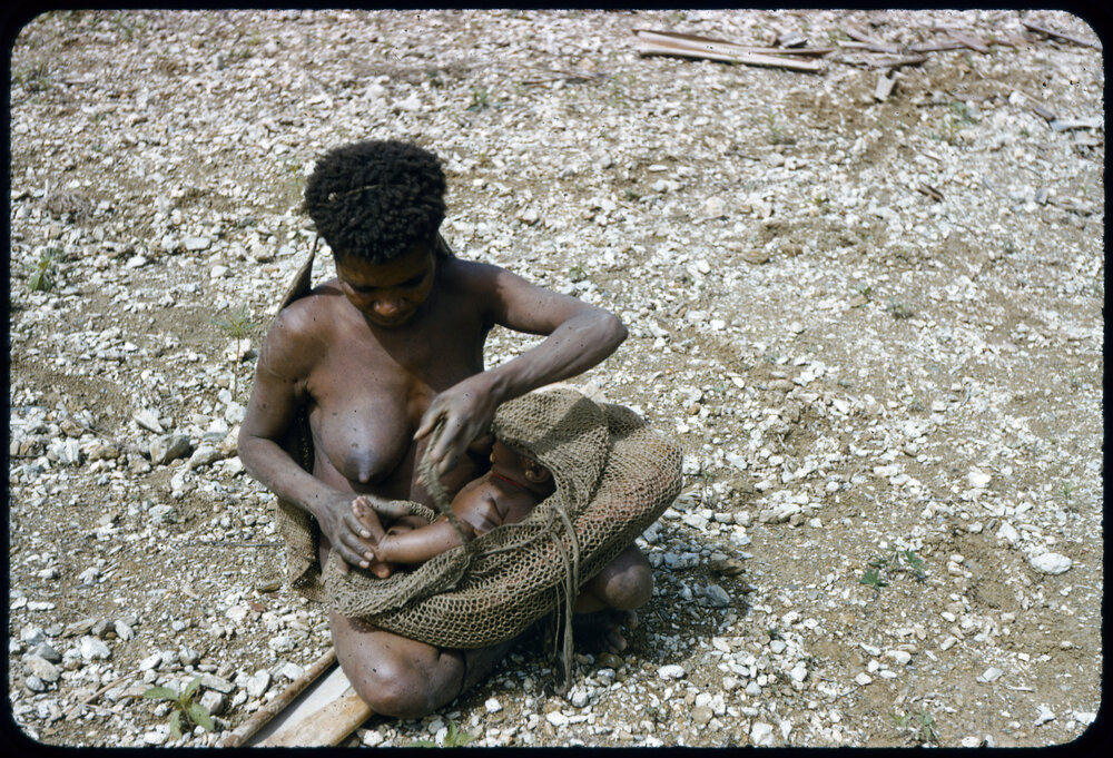 Woman Placing Child in Net Carrier
