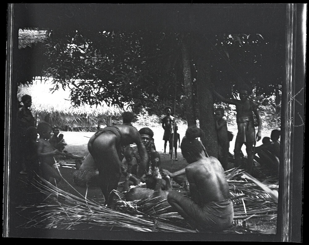 [Manum Island, New Guinea] Tiboiŋ and Others Cutting up Bazaba&rsquo;s Pig. Women Standing in Background