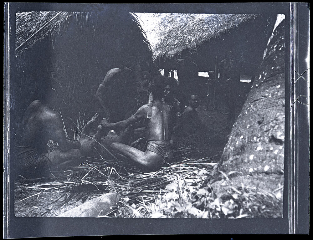 [Manum Island, New Guinea] Tiboiŋ and Others Cutting up Bazaba&rsquo;s Pig. Women Standing in Background