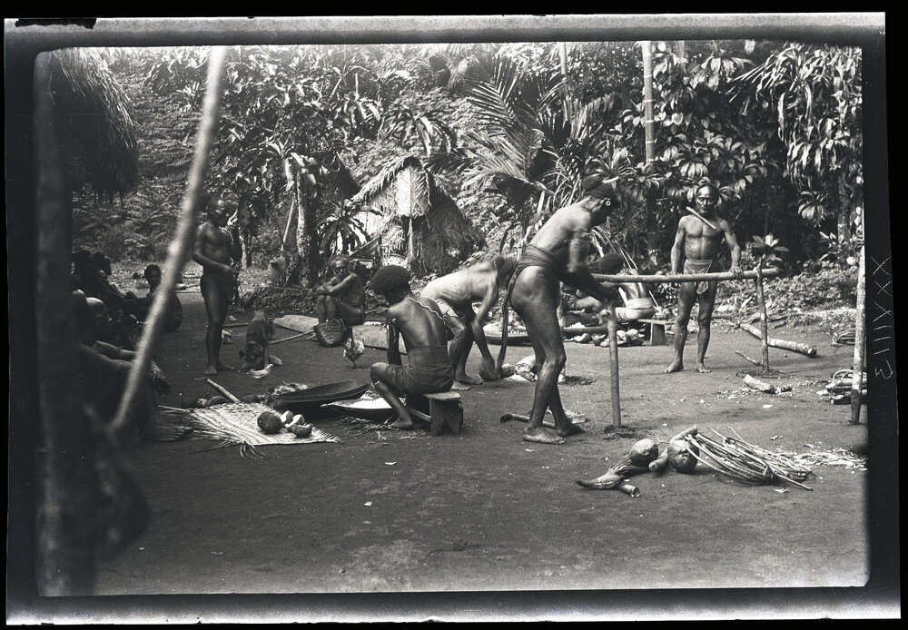 [Manum Island, New Guinea] Making the 'Bed'. Fixing the Transverse Posts. Other Men Scraping Coconuts or Just Sitting Looking On