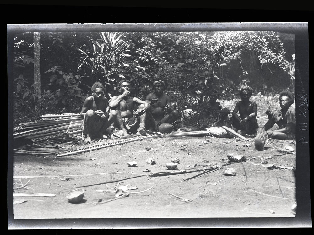 [Manum Island, New Guinea] Men who have Finished Plaiting Leaves, Sit Resting and Eating the Food Cooked in the Open Fire