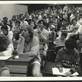 Students Attending an Overcrowded Lecture Sitting on Stairs, Standing at Back