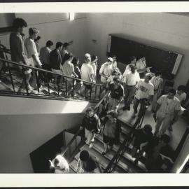 Students in Stairwell After Examination with Staff Member Holding a Sign 'Silence Examination in Progress'