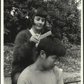 Outdoor Hairdressing - A Male Receives a Haircut by a Female Who Sits on a Wall Behind him