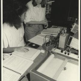 Physics Laboratory Two Students at a Desk Checking Papers