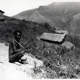 Man Crouching with Buildings on Mountainside in Background