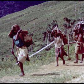 Women Carrying Net Bags Along Mountainside Path