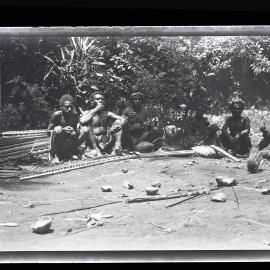 [Manum Island, New Guinea] Men who have Finished Plaiting Leaves, Sit Resting and Eating the Food Cooked in the Open Fire